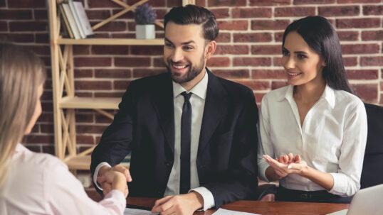 Pareja de asesores legales inmobiliarios en una oficina estrechando la mano de una clienta, simbolizando la firma de un acuerdo o contrato.