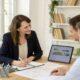 Gestor inmobiliario explicando a dos clientes las funciones relacionadas con contratos, finanzas y evaluación de propiedades durante una reunión en oficina.