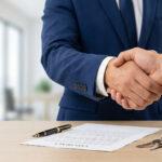 Primer plano de un apretón de manos sobre un escritorio con un contrato y llaves de una propiedad, representando el éxito de una transacción basada en la confianza profesional.